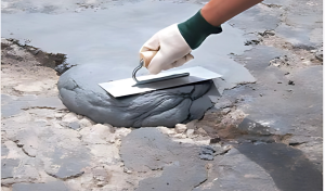 Mano aplicando mortero cementosos en asfalto para la reparación de juntas y baches.